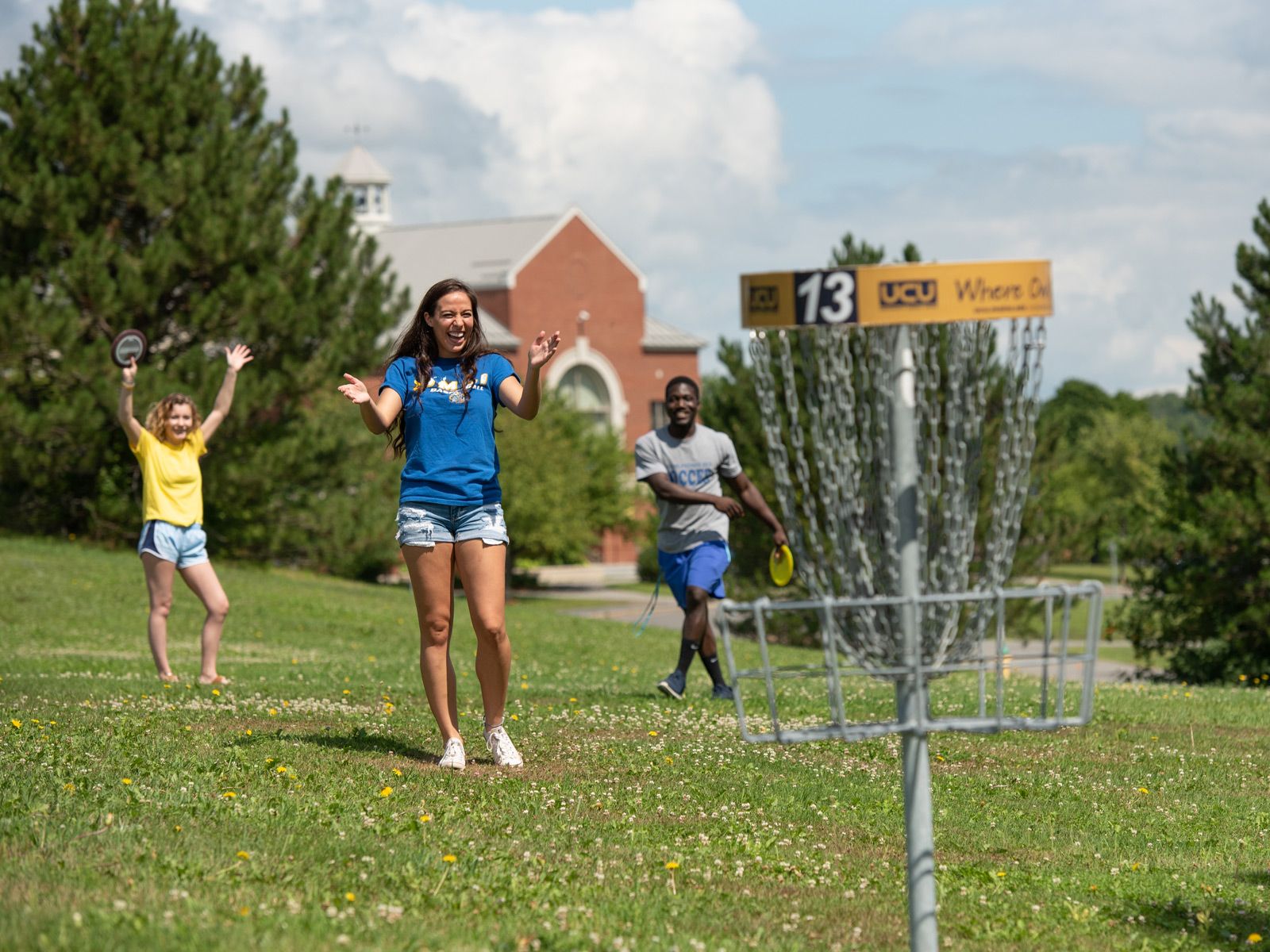 three students cheer while playing disc golf