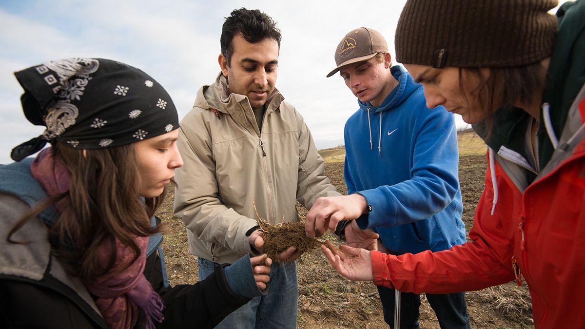 Instructor with students examining soil in a field